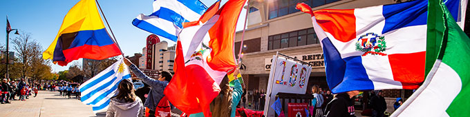 A parade with people holding various national flags outside a building with an Arizona State University sign.