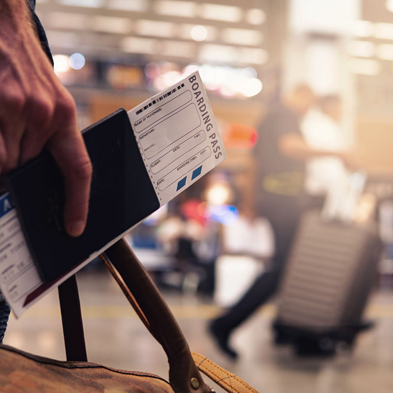 A man carrying a bag, holding his passport and airplane ticket at an airport.